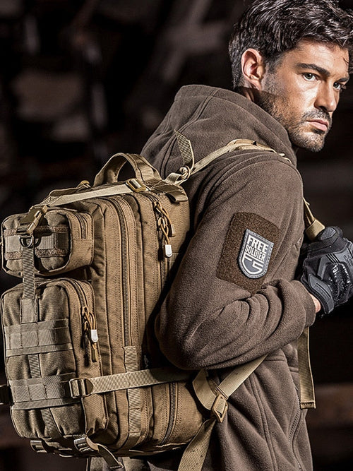 Man wearing a brown jacket with a tactical backpack and glove, against a dark background