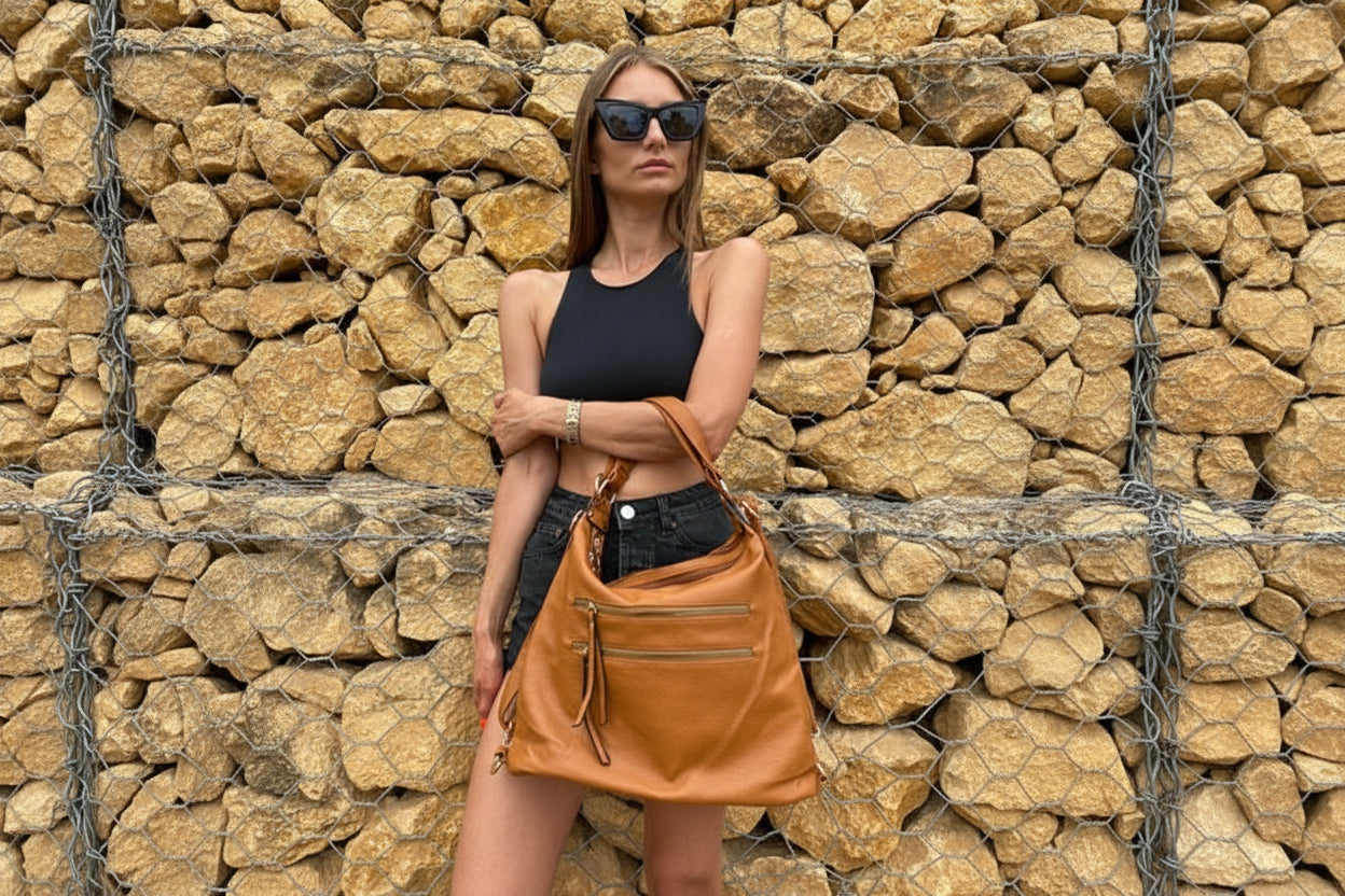 Woman holding a brown leather bag against a stone wall