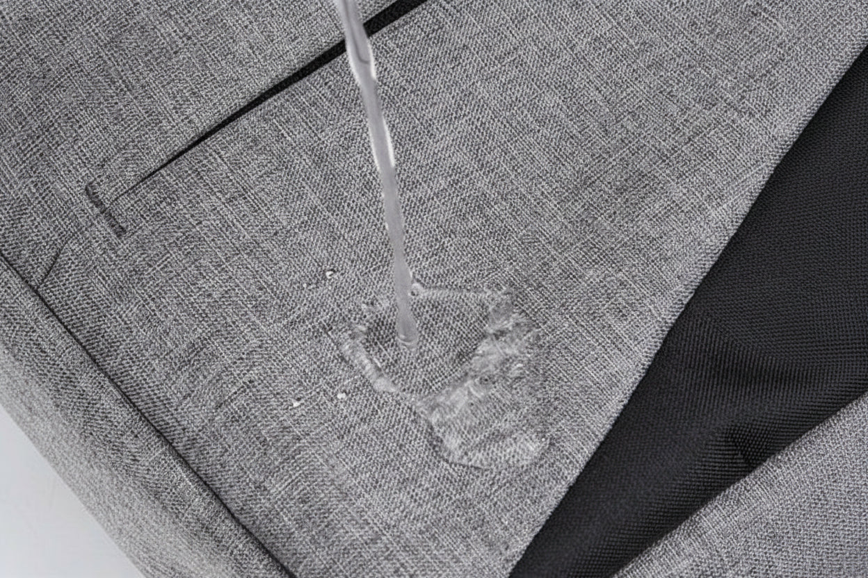 Gray fabric with water being poured onto it, demonstrating water resistance.