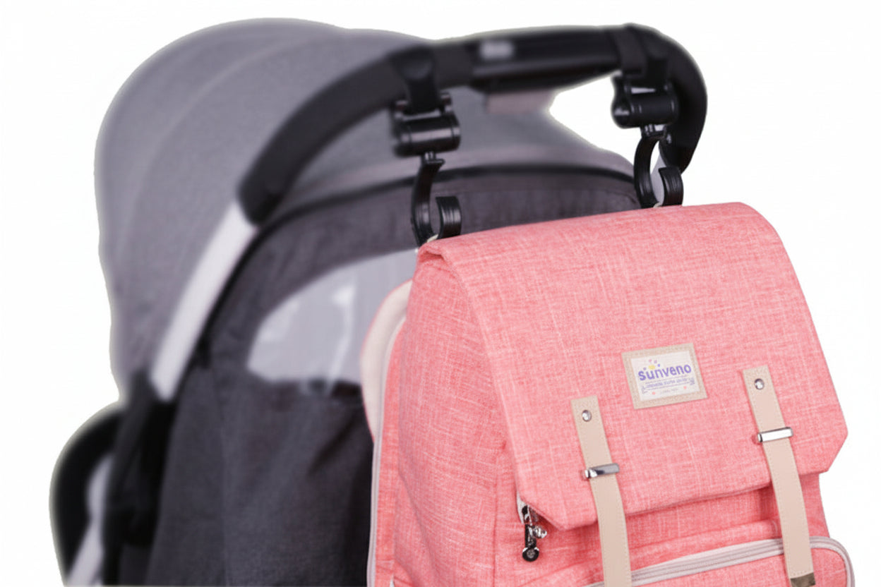 Pink backpack with beige straps attached to a black stroller on a white background
