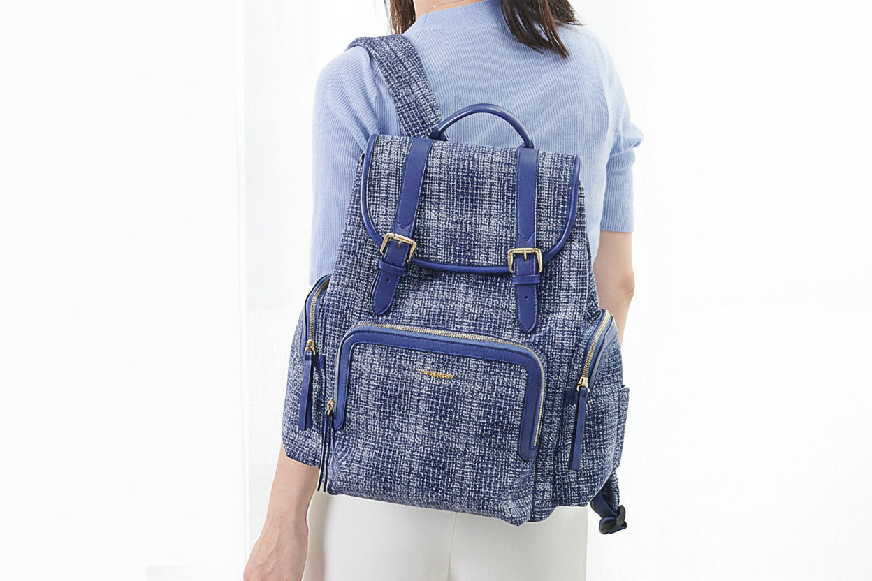 Person wearing a blue textured backpack with gold zippers on a white background